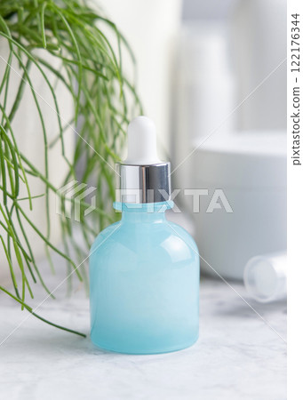 Light blue dropper bottle on marble near green plant and cosmetics close up, mockup 122176344