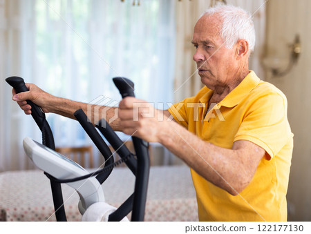 Old man using elliptic trainer at home Old man using elliptic trainer at home 122177130