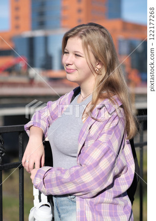 A blonde girl dressed casually smiles while standing outdoors, framed by a bright cityscape. This image reflects themes of individuality and optimism in a bustling environment. A blonde girl dressed casually smiles while standing outdoors, framed by a bright cityscape. This image reflects themes of individuality and optimism in a bustling environment. 122177268