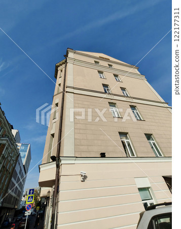 A beige facade with wrought iron canopies, wooden doors, and clean windows along a paved sidewalk. The photo showcases urban architecture combining traditional elements with modern simplicity. 122177311