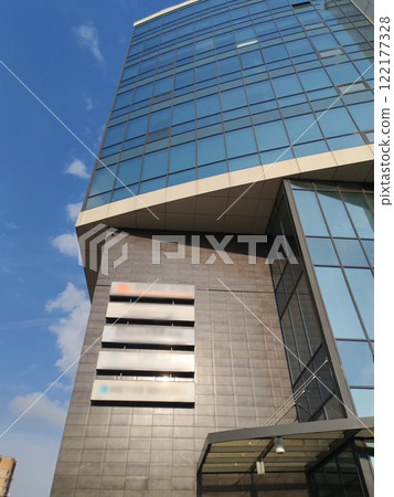 A modern multi-story building with a sleek, geometric facade and large glass windows. The minimalist architectural design emphasizes clean lines and contemporary urban development in a growing city. 122177328