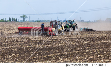 Farmers using tractors to plant seeds in a large field on a sunny day 122180112