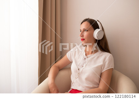 Woman enjoying music while sitting in a cozy chair by the window Woman enjoying music while sitting in a cozy chair by the window 122180114
