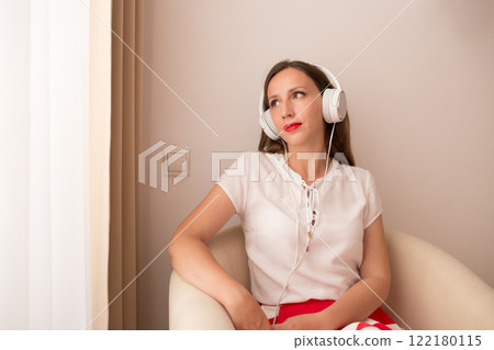 Woman enjoying music while sitting in a cozy chair by the window 122180115