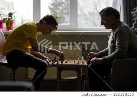 Young boy playing chess with his grandfather indoors during a quiet afternoon Young boy playing chess with his grandfather indoors during a quiet afternoon 122180130
