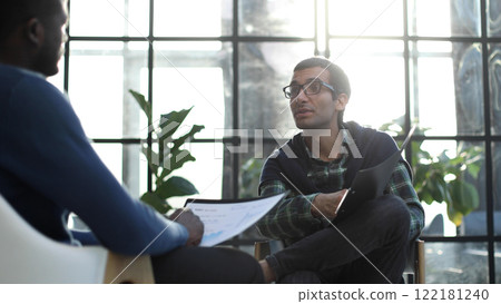 Thoughtful business man in formalwear holding paper while sitting at chair fills out a resume questionnaire in office 122181240