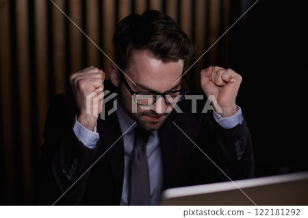 Portrait of a young man sitting in front of a laptop happy and excited, raising his hands 122181292