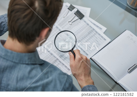 Businessman looking through a magnifying glass to documents note in the office. Businessman looking through a magnifying glass to documents note in the office. 122181582