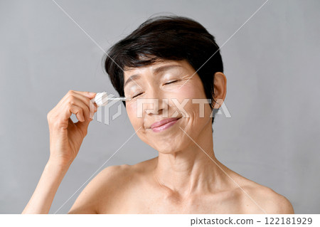 一名中年亞洲女性用滴管將血清塗抹在臉上 一名中年亞洲女性用滴管將血清塗抹在臉上 122181929