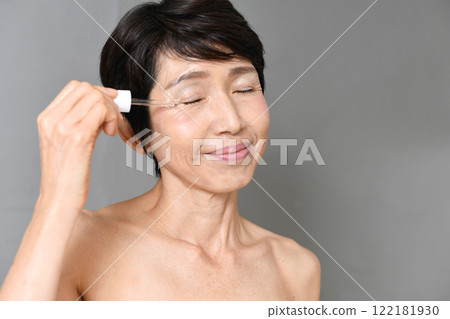 一名中年亞洲女性用滴管將血清塗抹在臉上 一名中年亞洲女性用滴管將血清塗抹在臉上 122181930