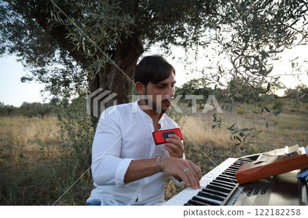 Boy Plays Music With Harmonica And Keyboard Among The Olive Trees Of Calabria 122182258