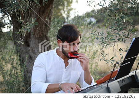 Boy Plays Music With Harmonica And Keyboard Among The Olive Trees Of Calabria Boy Plays Music With Harmonica And Keyboard Among The Olive Trees Of Calabria 122182262
