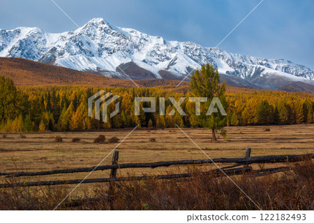 Snowcapped mountain with autumn forest and wooden fence under cloudy sky Snowcapped mountain with autumn forest and wooden fence under cloudy sky 122182493