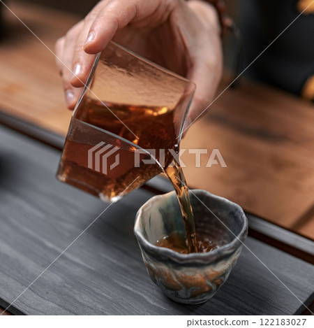 Pouring a delightful and aromatic tea into an elegant ceramic cup enhances the experience Pouring a delightful and aromatic tea into an elegant ceramic cup enhances the experience 122183027