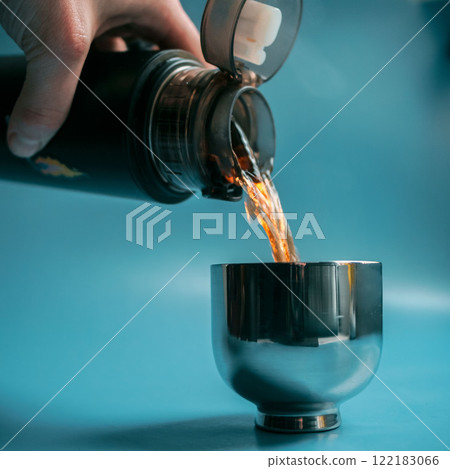 Pouring a refreshing beverage from a thermos into a stylish metal cup for enjoyment outside Pouring a refreshing beverage from a thermos into a stylish metal cup for enjoyment outside 122183066