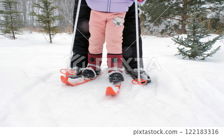 Young mother gently guides her daughter through her first skiing experience, with the excited girl holding onto her poles, ready to glide on the slopes Young mother gently guides her daughter through her first skiing experience, with the excited girl holding onto her poles, ready to glide on the slopes 122183316