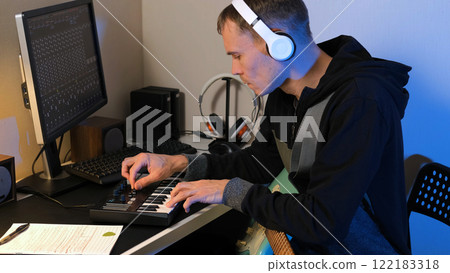 Skilled musician sits at a desk in a cozy home studio, passionately creating music using a MIDI keyboard while holding a mint electric guitar 122183318