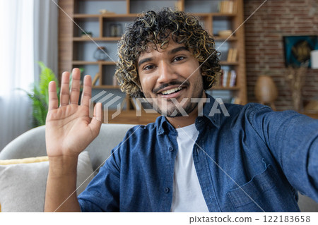 A man looks into the phone camera, happily waves his hand, takes a selfie photo and talks to colleagues and friends remotely using a smartphone app for video chats. 122183658