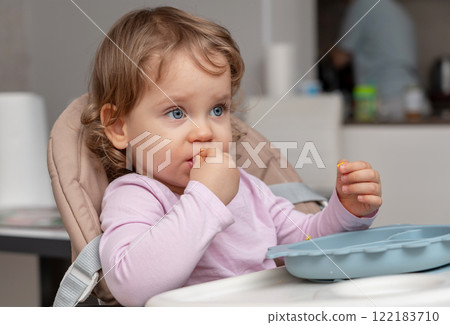 A confident toddler enjoying self-feeding during an independent mealtime experience. A confident toddler enjoying self-feeding during an independent mealtime experience. 122183710