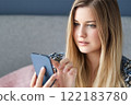 Woman with long blonde hair and blue eyes looking at her smartphone, online shopping, work from home lifestyle idea 122183780