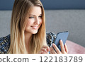 Woman with long blonde hair and blue eyes looking at her smartphone, online shopping, work from home lifestyle idea 122183789