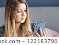Woman with long blonde hair and blue eyes looking at her smartphone, online shopping, work from home lifestyle idea 122183790