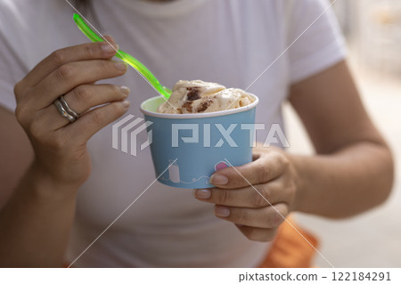 a woman in a white T-shirt eats ice cream from a paper cup with a spoon, summer, heat 122184291