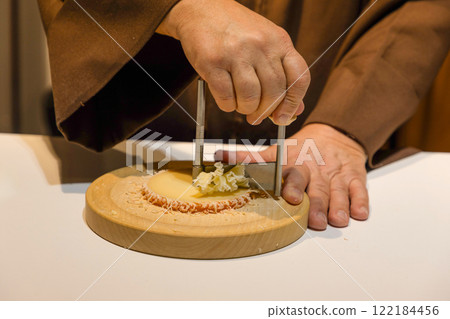 middle section of a middle aged man with hands in monk's robe cutting cheese 122184456