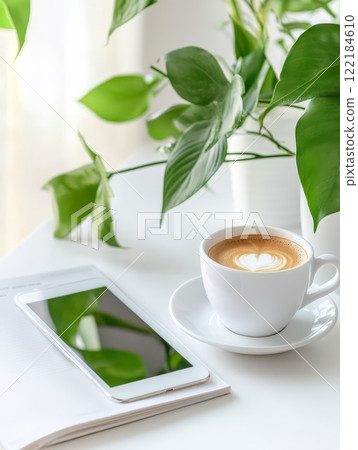 A tablet and a cup of coffee on a desk, complemented by fresh white flowers, representing a serene workspace setup A tablet and a cup of coffee on a desk, complemented by fresh white flowers, representing a serene workspace setup 122184610