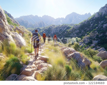 Hikers explore rocky trail surrounded by mountains and greenery in bright sunlight during afternoon adventure Hikers explore rocky trail surrounded by mountains and greenery in bright sunlight during afternoon adventure 122184669