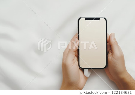 Two hands holding a smartphone with a blank screen on a white surface, emphasizing focus on the device, ideal for technology and app presentation concepts 122184681