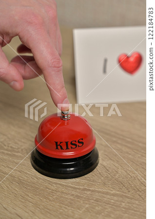 Man's finger presses the red bell, ring for kiss, Valentine's Day greeting card romantic letter with heart on wooden table. Preparation to celebration 122184783