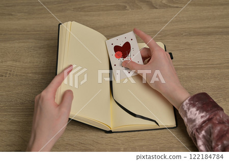 Woman's hands found Valentine's Day greeting card romantic letter with red heart in a notebook on wooden table 122184784