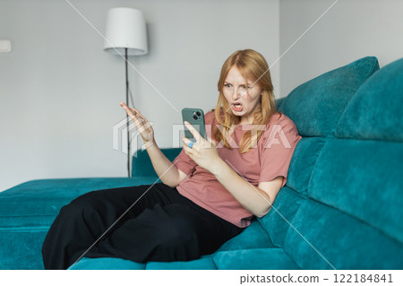 Upset sad, skeptical, serious woman holding smartphone gadget for communicate indoors. Negative people emotion, pensive girl sitting on floor at home. 30s woman holding smartphone. Screaming, hate. 122184841