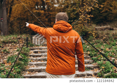 Blonde male pointing finger outdoors, he hiking on woodland, rear view. Active lifestyle concept. Trip, travel and people banner. High quality photo 122184842