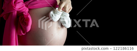 Pregnant woman holding a small pair of white booties 122186116