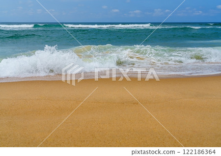 Sandy beach with gentle waves lapping at the shore under a blue sky 122186364