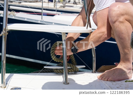 Close-up of a man s hand untying a rope on a cleat on a boat deck at the marina while barefoot. 122186395
