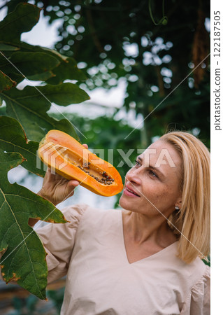 Woman examining ripe papaya in a lush garden during daytime Woman examining ripe papaya in a lush garden during daytime 122187505