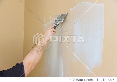 Worker is applying drywall compound to wall, preparing it for painting in residential living space. 122188907
