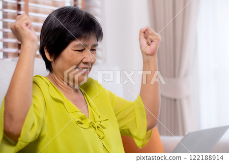 Asian senior woman sitting on sofa using laptop computer for looking social media with success. Asian senior woman sitting on sofa using laptop computer for looking social media with success. 122188914