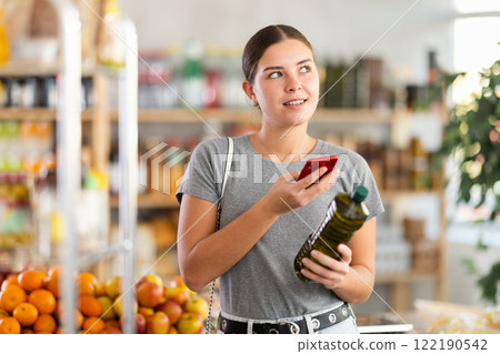 In shop youth girl scan QR code and take reading olive oil package bottle using phone camera In shop youth girl scan QR code and take reading olive oil package bottle using phone camera 122190542