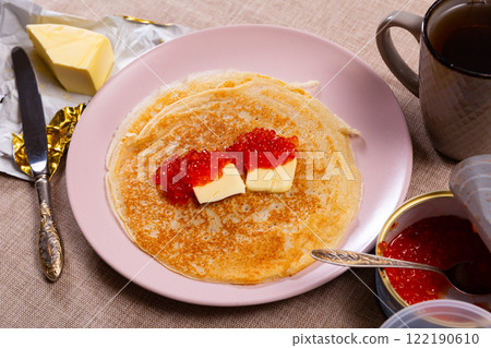 Tasty russian pancakes with piece of butter and red caviar at plate 122190610