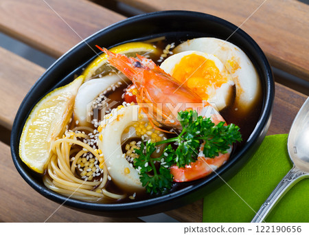 Spicy pan-Asian soup with squid, shrimp, egg noodles and sesame is tasty dish 122190656