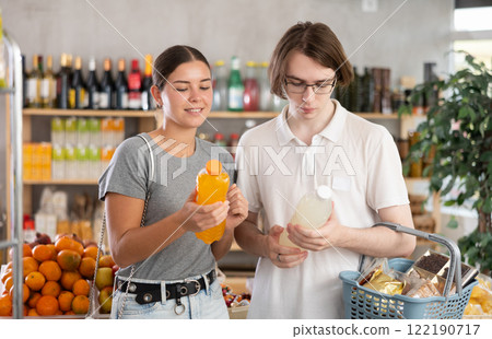 Youth girl and guy friends hold packages bottles and choose consider drink in store Youth girl and guy friends hold packages bottles and choose consider drink in store 122190717