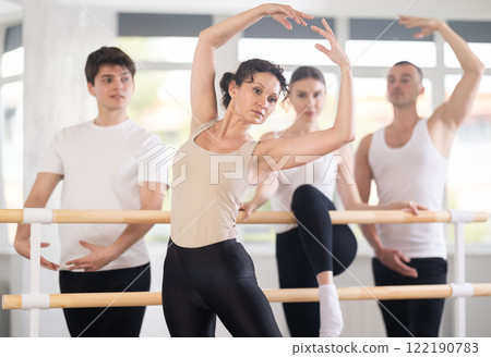 Beautiful young woman ballerina posing with group of dancers in ballet training hall Beautiful young woman ballerina posing with group of dancers in ballet training hall 122190783