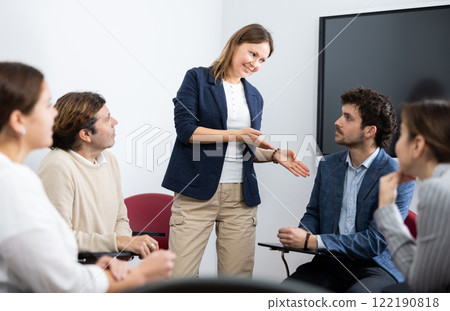 Positive successful female teacher listening to answers from students of different ages while they sitting in circle at foreign language lesson 122190818