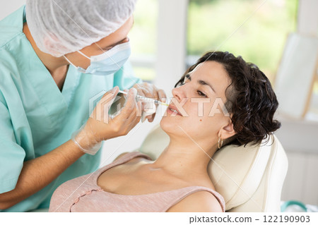 Middle-aged woman having face care by means of injection in aesthetic clinic Middle-aged woman having face care by means of injection in aesthetic clinic 122190903