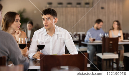 Three friends meeting in modern restaurant - men and woman drinking wine, talking, discussing problems Three friends meeting in modern restaurant - men and woman drinking wine, talking, discussing problems 122190958