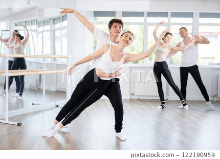 Acrobatic couple perform ballet pose with support during group training class in ballet hall Acrobatic couple perform ballet pose with support during group training class in ballet hall 122190959